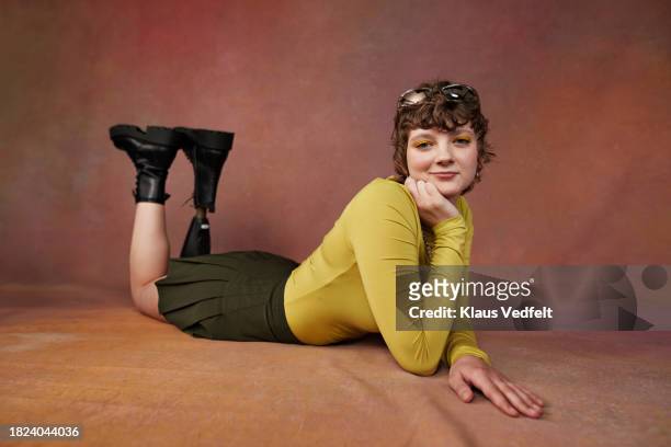 portrait of girl having disabilities with hand on chin lying in front of brown backdrop - brown shoe stock pictures, royalty-free photos & images