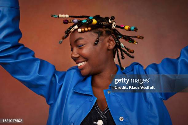 happy teenage girl wearing blue jacket shaking head against brown background - braid hairstyle stock pictures, royalty-free photos & images