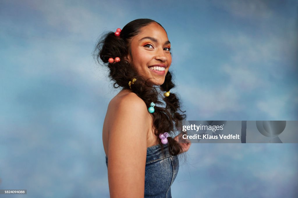 Side view of happy teenage girl with braided hair looking away by colored background