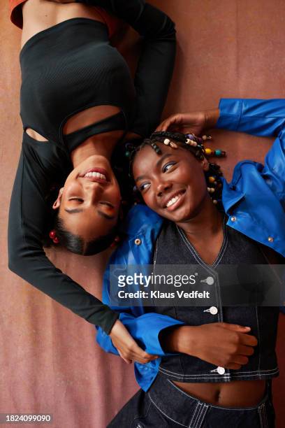 teenage multiracial female friends lying down on brown backdrop - hands on tummy stock pictures, royalty-free photos & images