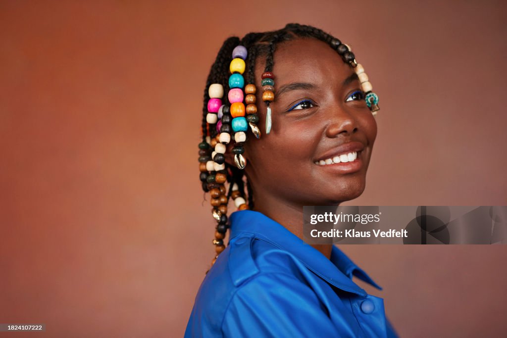 Smiling teenage girl looking away while day dreaming by brown background