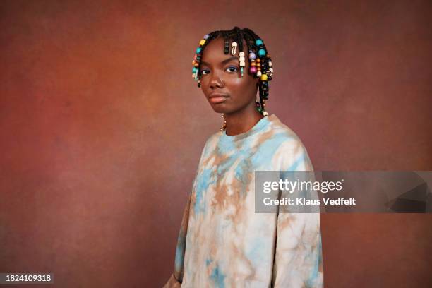 portrait of serious teenage girl with beads on braids standing against brown background - white bead stock pictures, royalty-free photos & images