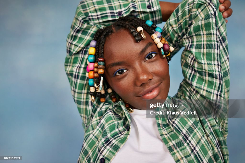 Portrait of teenage girl wearing plaid shirt with hands behind head against colored background