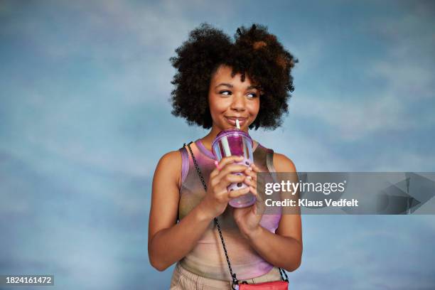 portrait of afro teenage girl drinking water while standing against colored background - sly smile girl stock pictures, royalty-free photos & images
