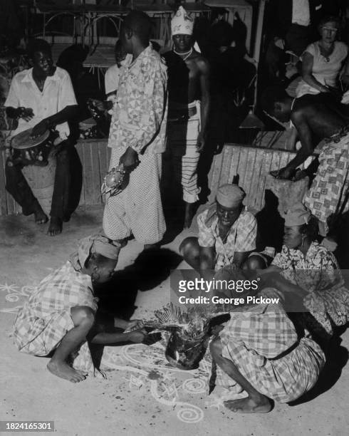 Group of people crouch around a chicken, as the animal is sacrificed during a voodoo ceremony in Haiti, circa 1955. Haiti is on the island of...