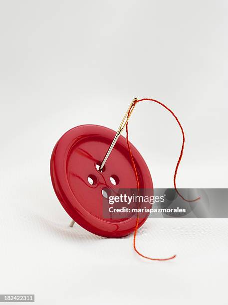 red button with four thread holes and a needle with thread - button concept stock pictures, royalty-free photos & images