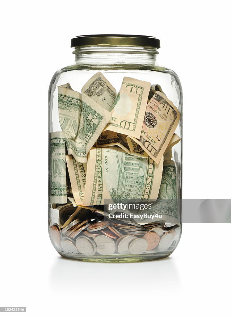 A clear glass jar filled with cash and coins 