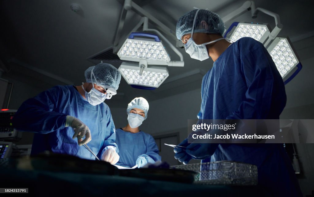 Teamwork, emergency and doctors or people in surgery procedure or healthcare operation in hospital. Night, low angle or surgeon in face mask or gloves help in dark operating room in medical clinic