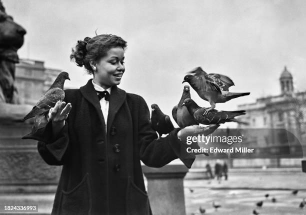 American actress Isabel Cooley feeding pigeons in Trafalgar Square, London, March 13th 1953. Cooley is in London to appear in the Negro Players...