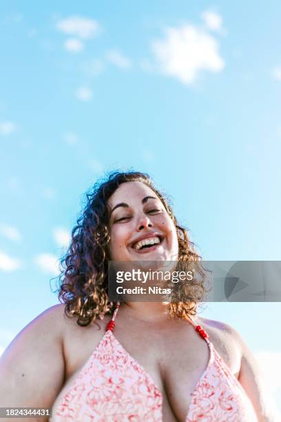 portrait of plus size beutiful curly woman on blue sky background - curvy model stock-fotos und bilder