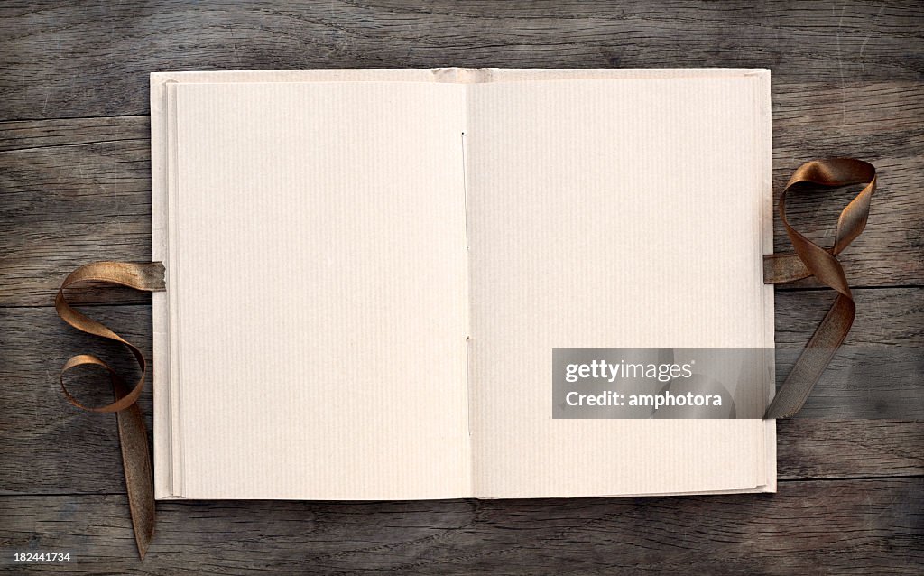 Open blank book on dark wooden table with a brown ribbon