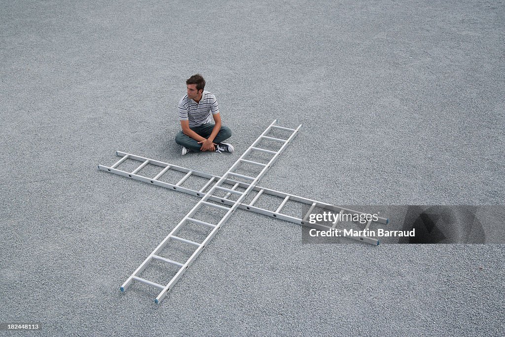 Man sitting cross legged outdoors with two ladders