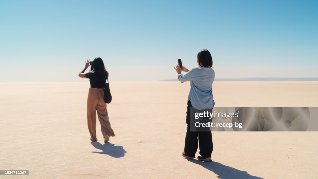 Two female multi-ethnic friend tourists exploring and taking photos and videos in Tuz Gölü Salt Lake in Anatolia region of Türkiye Turkey