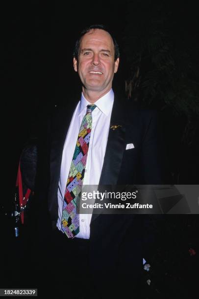 British actor and comedian John Cleese, wearing a multi-coloured necktie with the design being a collage of ticket stubs, with a white shirt beneath...