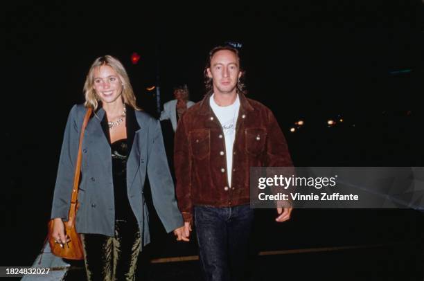 British actress Olivia d'Abo, wearing a grey jacket, holding hands with British singer and musician Julian Lennon, who wears a brown jacket, in Los...