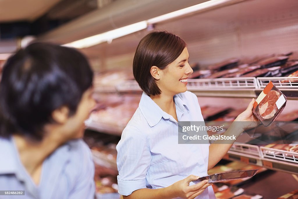 Glückliches Paar, die ein Paket von Fleisch im Supermarkt