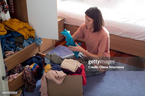 woman sorting out the clothes in the wardrobe and sorting for second hand - dragen stockfoto's en -beelden