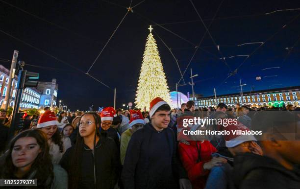 People wear Santa hats as a crowd gathers to watch fireworks and laser show during the lighting of a large Christmas tree and buildings in Praça do...