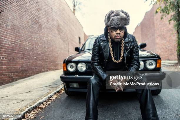 man in old school hip hop clothing sitting on classic car - hip hop foto e immagini stock