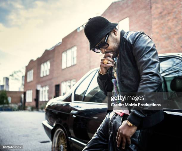 man in hip hop clothing leaning against classic car - music from the motor city stock pictures, royalty-free photos & images