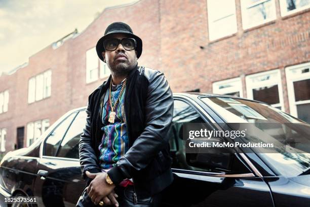 man in old school hip hop clothing leaning against classic car - gold chain necklace stock pictures, royalty-free photos & images