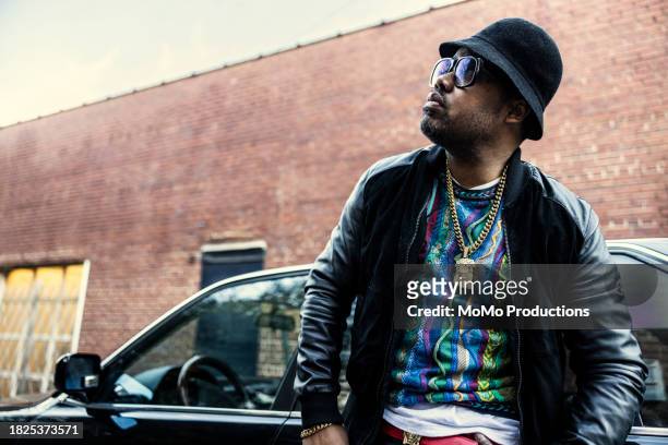 man in old school hip hop clothing leaning against classic car - music from the motor city stock pictures, royalty-free photos & images