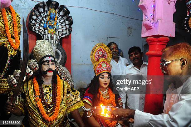 An Hindu devotee performs 'Arti' as he offers prayers to an artist dressed as demon king Ravana ahead of a religious procession Ravan ki Barat in...