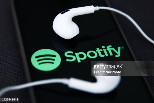 Headphones and Spotify logo displayed on a phone screen are seen in this illustration photo taken in Krakow, Poland on December 5, 2023.