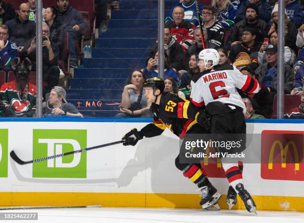John Marino of the New Jersey Devils checks Teddy Blueger of the Vancouver Canucks during the second period of their NHL game at Rogers Arena on...