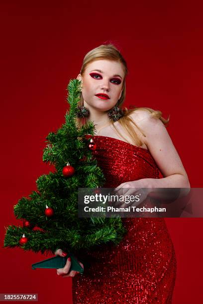 beautiful woman wearing red dress holding christmas tree - form fitted dress stock pictures, royalty-free photos & images