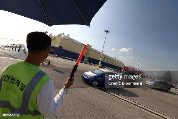 Worker directs Kia Motors Corp. Vehicles bound for export at the port of Pyeongtaek in Pyeongtaek, South Korea, on Monday, Sept. 30, 2013. South...