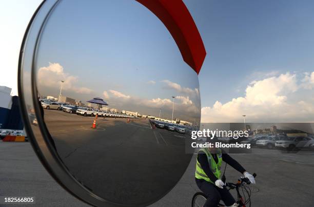 Worker rides a bicycle past a mirror reflecting Kia Motors Corp. Vehicles bound for export at the port of Pyeongtaek in Pyeongtaek, South Korea, on...
