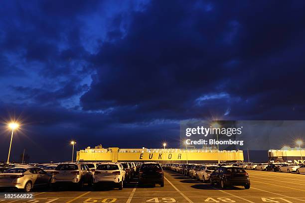 Kia Motors Corp. Vehicles bound for export await shipment in front of a Eukor Car Carriers Inc. Roll-on/roll-off cargo ship at dusk at the port of...