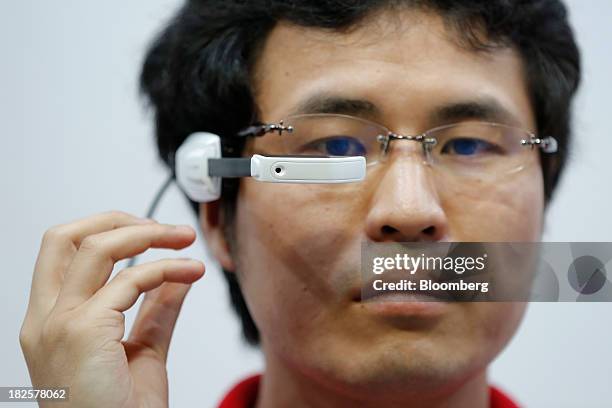Booth attendant adjusts NTT DoCoMo Inc.'s Intelligent Glass wearable device as he demonstrates the device at the CEATEC Japan 2013 exhibition in...