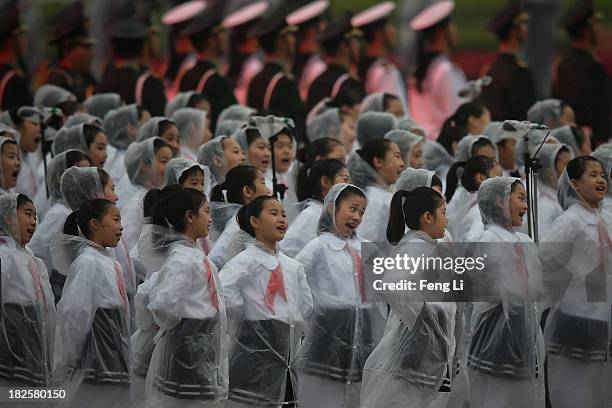 Chinese students wearing raincoats perform for a tribute ceremony marking the 64th anniversary of the founding of the People's Republic of China at...
