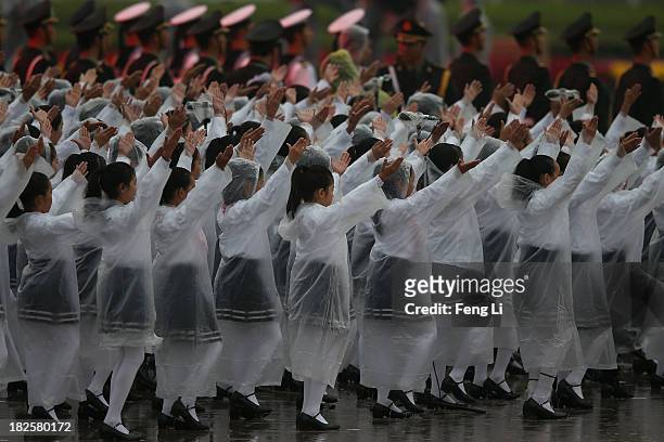 Chinese students wearing raincoats perform for a tribute ceremony marking the 64th anniversary of the founding of the People's Republic of China at...