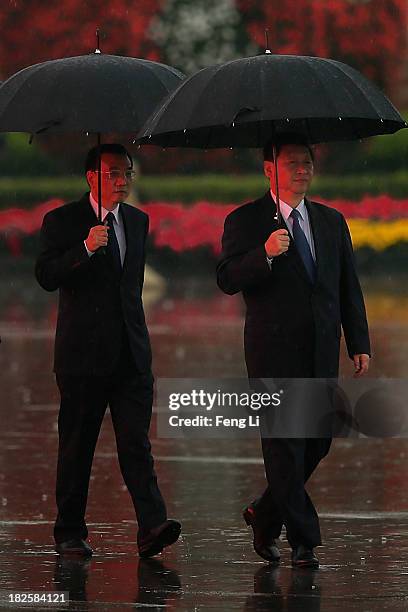 Chinese President Xi Jinping and Premier Li Keqiang hold umbrellas as they arrive for a tribute ceremony marking the 64th anniversary of the founding...