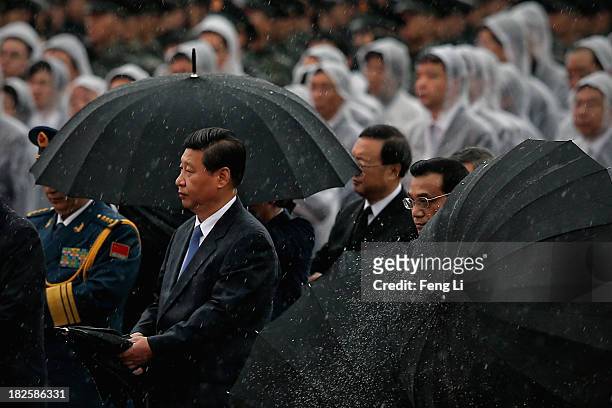 Chinese President Xi Jinping and Premier Li Keqiang open their umbrellas in the rain after bowing before the Monument to the People's Heroes during a...