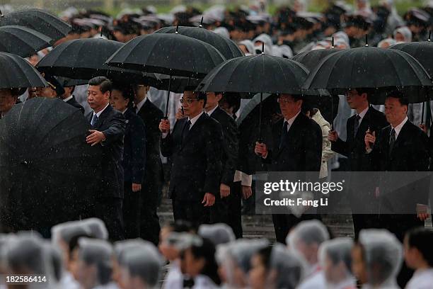 Chinese President Xi Jinping opens his umbrella as Premier Li Keqiang, members of the Politburo Standing Committee Yu Zhengsheng and Wang Qishan...