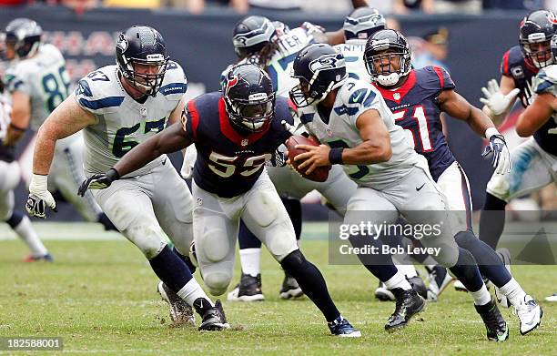 Russell Wilson of the Seattle Seahawks is pursued by Whitney Mercilus of the Houston Texans and Darryl Sharpton of the Houston Texans at Reliant...