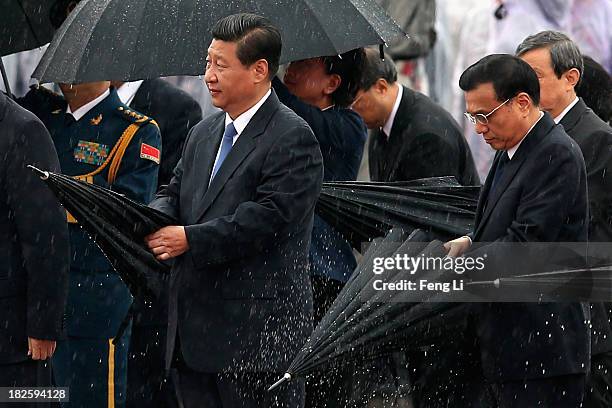 Chinese President Xi Jinping and Premier Li Keqiang close their umbrellas in the rain before bowing to the Monument to the People's Heroes during a...