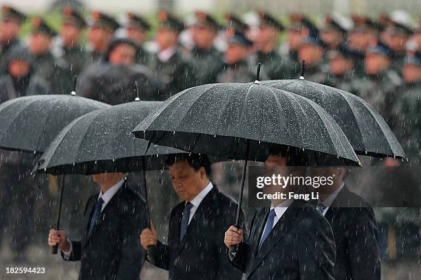 Chinese President Xi Jinping and Chinese Communist Party top leaders hold their umbrellas in the rain as they walk to the Monument to the People's...