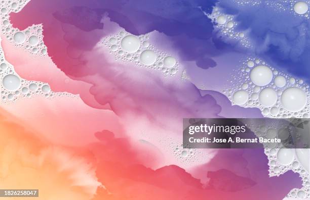 drops and splashes of orange and lilac paint with small bubbles of white liquid slide and mix. - bubble stock pictures, royalty-free photos & images