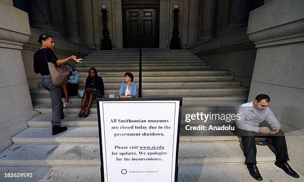 Employees of the Smithsonian Museum sit outside the museum behind a sign announcing the closing of museum due to the government shutdown on 1 October...