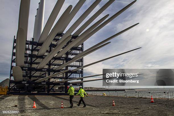 Workers pass wind turbine blades, manufactured by Vestas Wind Systems A/S, as they sit at the harbor at the company's pre-assembly facility in...