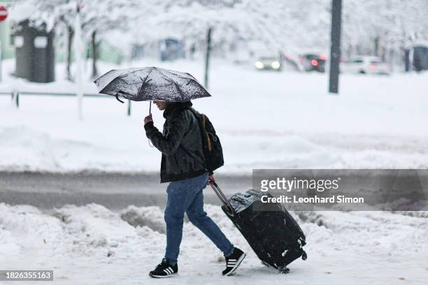 Man is crosses the street with a suitcase close to the train station of Moosach following a heavy snowfall on December 02, 2023 in Munich, Germany. A...