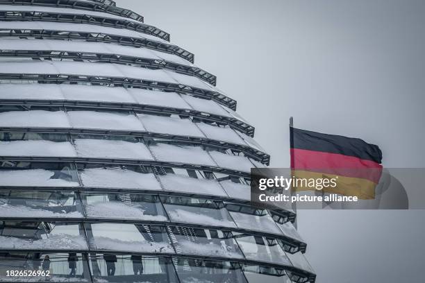 December 2023, Berlín: The German flag flies over the snow-covered dome of the Reichstag . Photo: Kay Nietfeld/dpa