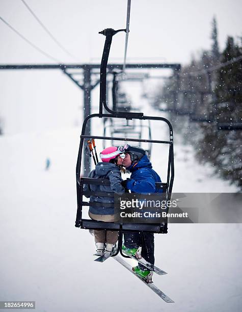 a couple share a kiss on a chairlift in softly falling snow. - couple ski lift stockfoto's en -beelden