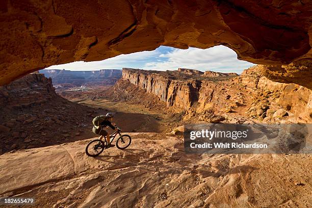 a mountain biker rides by on slickrock with dramatic desert scenery in the background. - moab utah fotografías e imágenes de stock