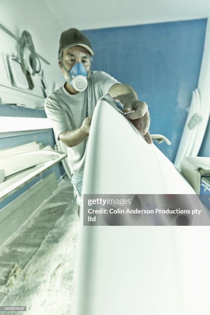 Craftsman sanding surfboard in workshop